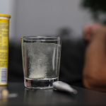 Effervescent tablet dissolving in glass, surrounded by medications, provides a healthcare-focused scene.